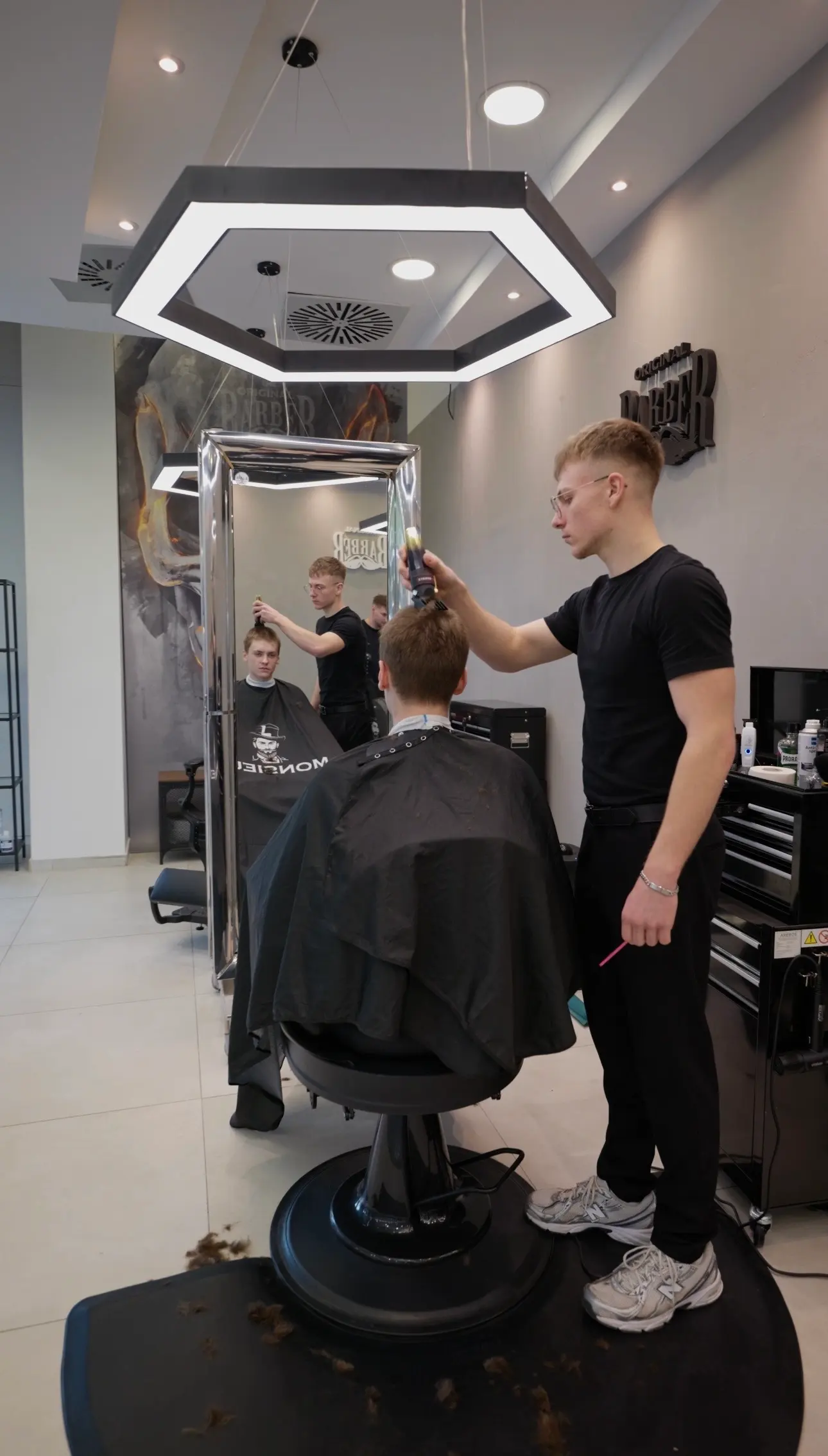Mladý barber upravuje klientovi vlasy pod nápisem Barber na zdi