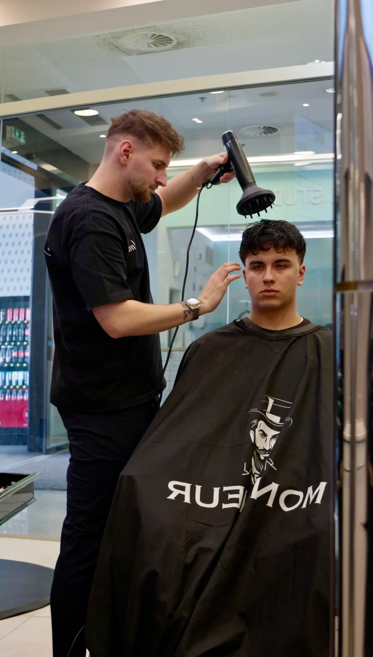 Barber fénuje klientovi vlasy v pláštěnce se štítkem Monsieur